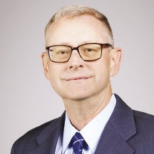 A man with glasses and a blue jacket and tie looks at the camera.