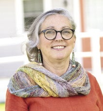A woman with glasses wearing a red shirt and scarf smiles at the camera.