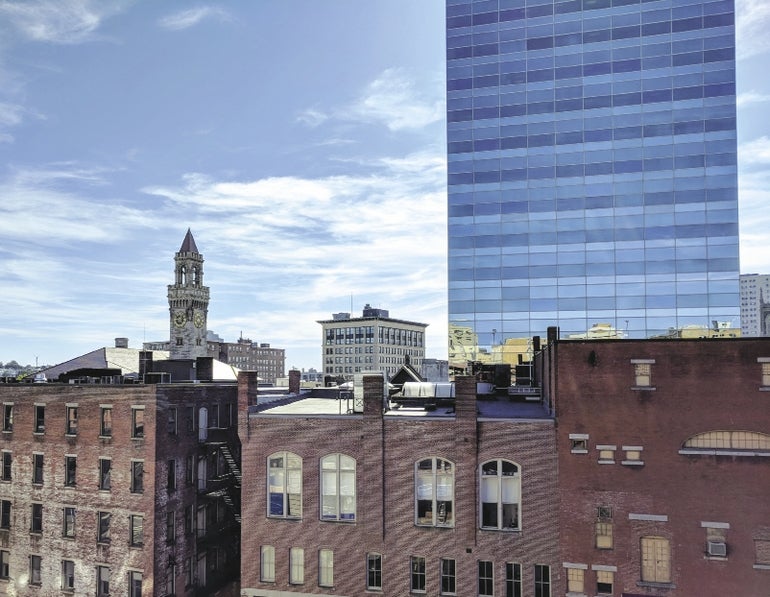 Worcester's skyline, with smaller brick facade buildings in front of a glass skyscraper and City Hall's clock tower. 