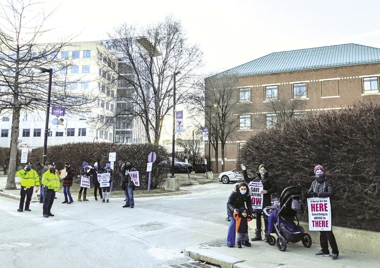 A group of people holding signs and police officers stand on a sidewalk in front of a large building.