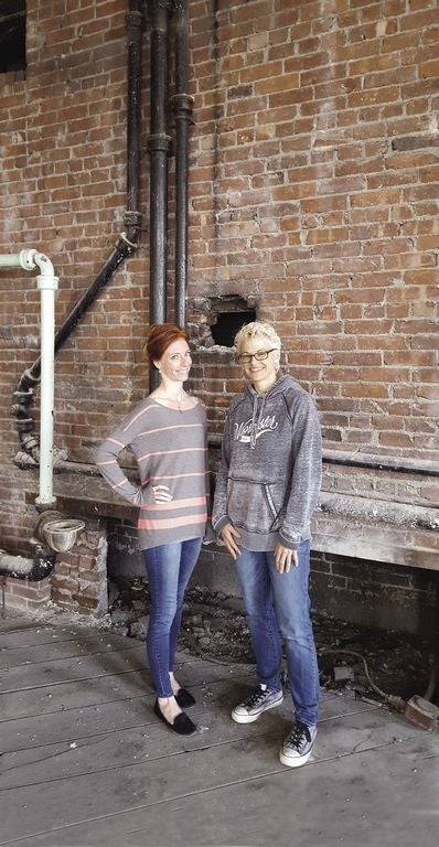 Two women stand together in a rundown building.