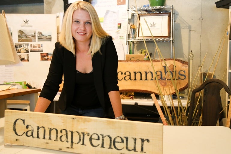 A woman stands in front of a sign saying cannapreneur.