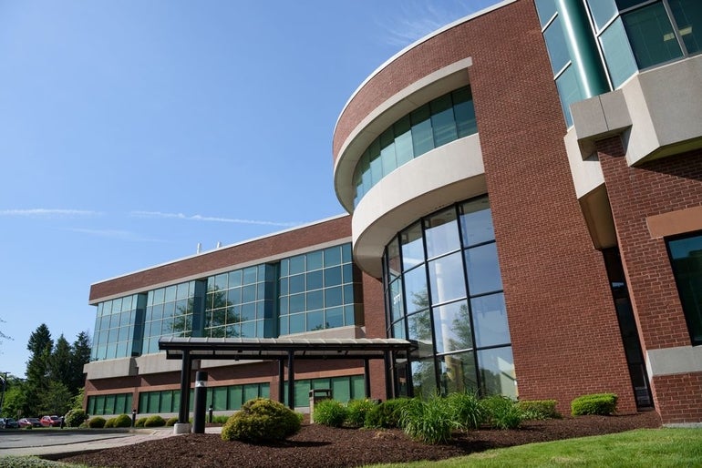 A brick and glass building with green shrubs in front.
