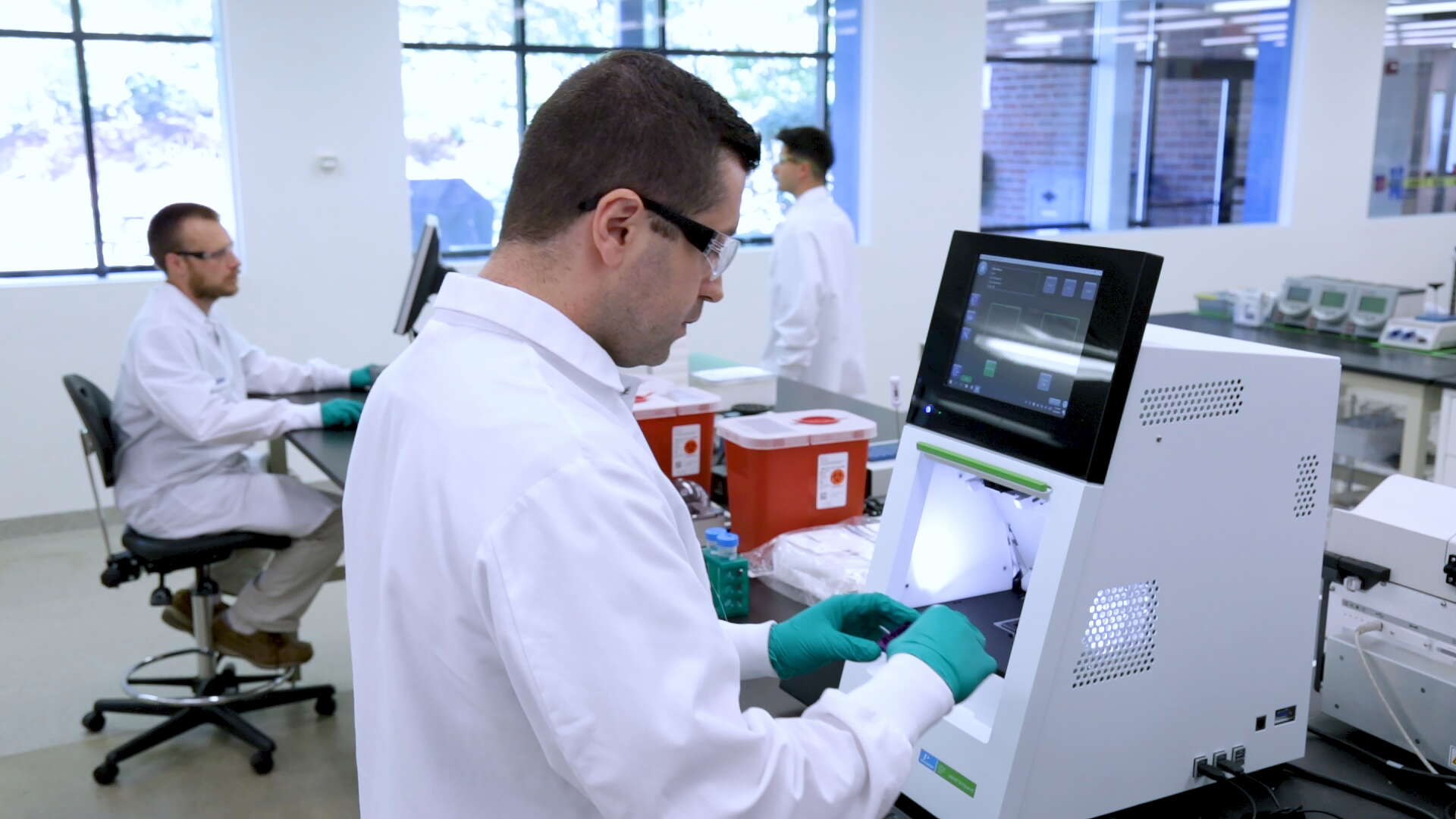 Workers wearing white lab coats and glasses work in a laboratory space