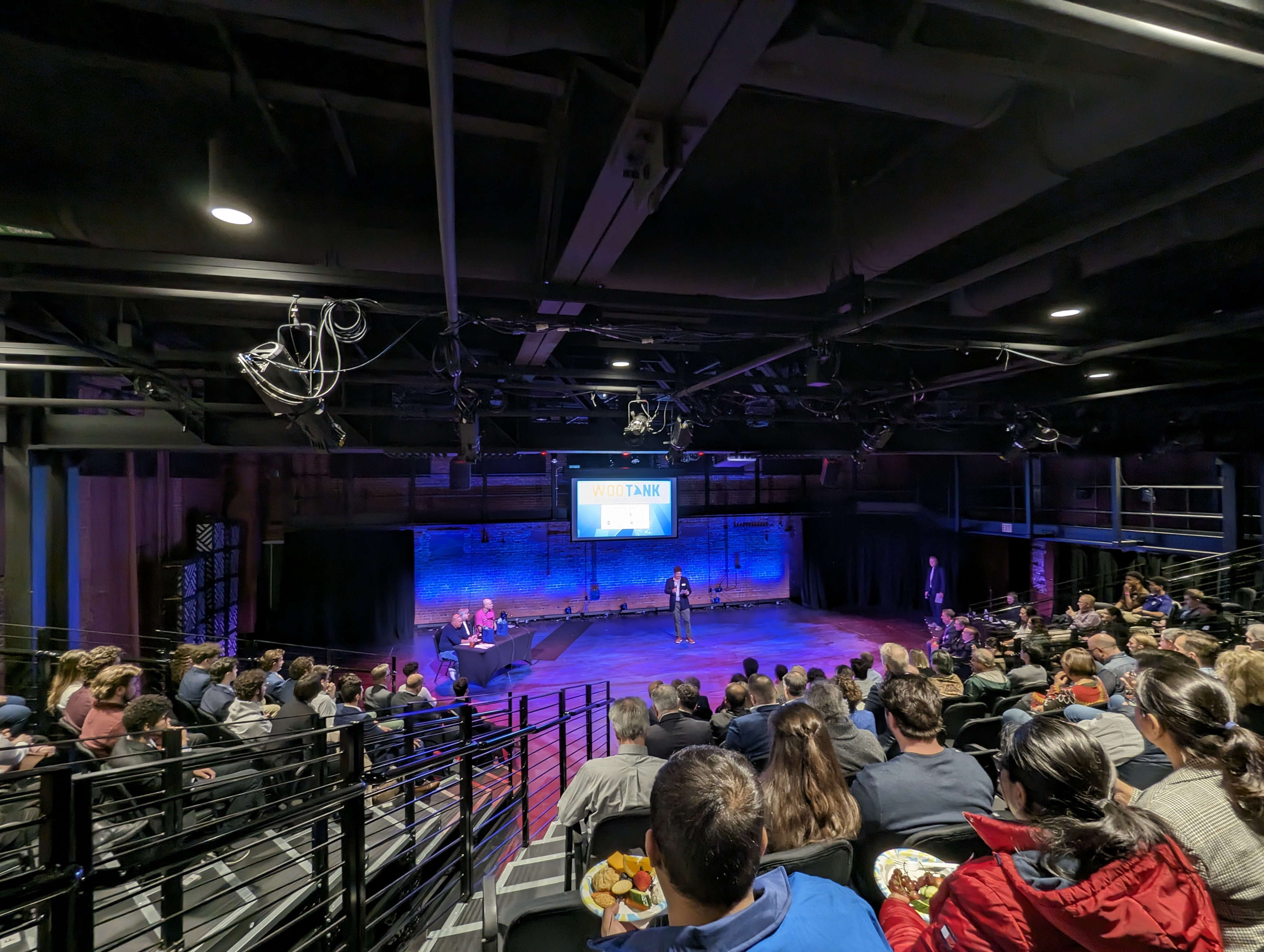 A wide-angle photo of a crowd of people seated in a theater. 