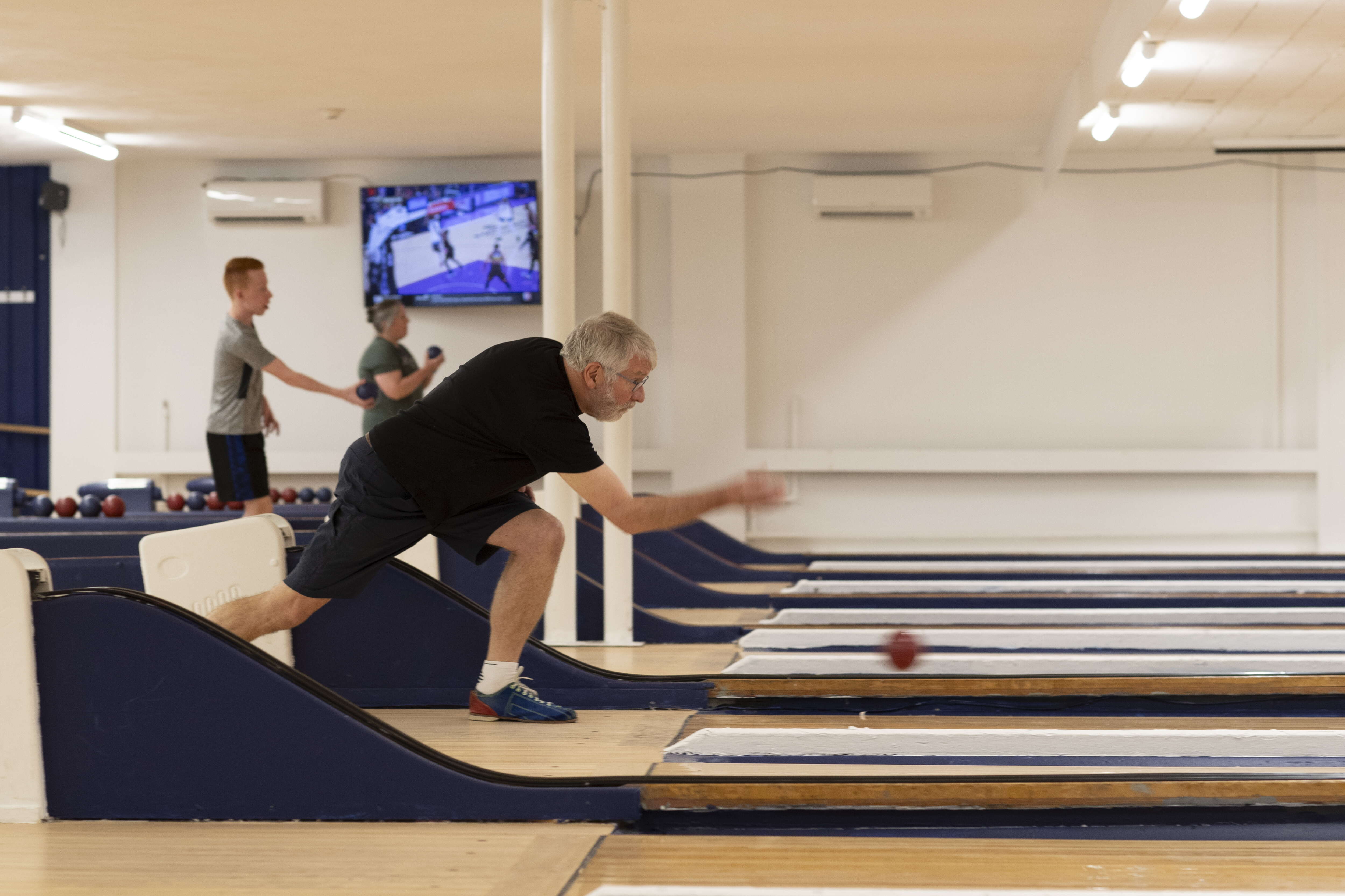 A man bowls a candlepin ball from a side angle