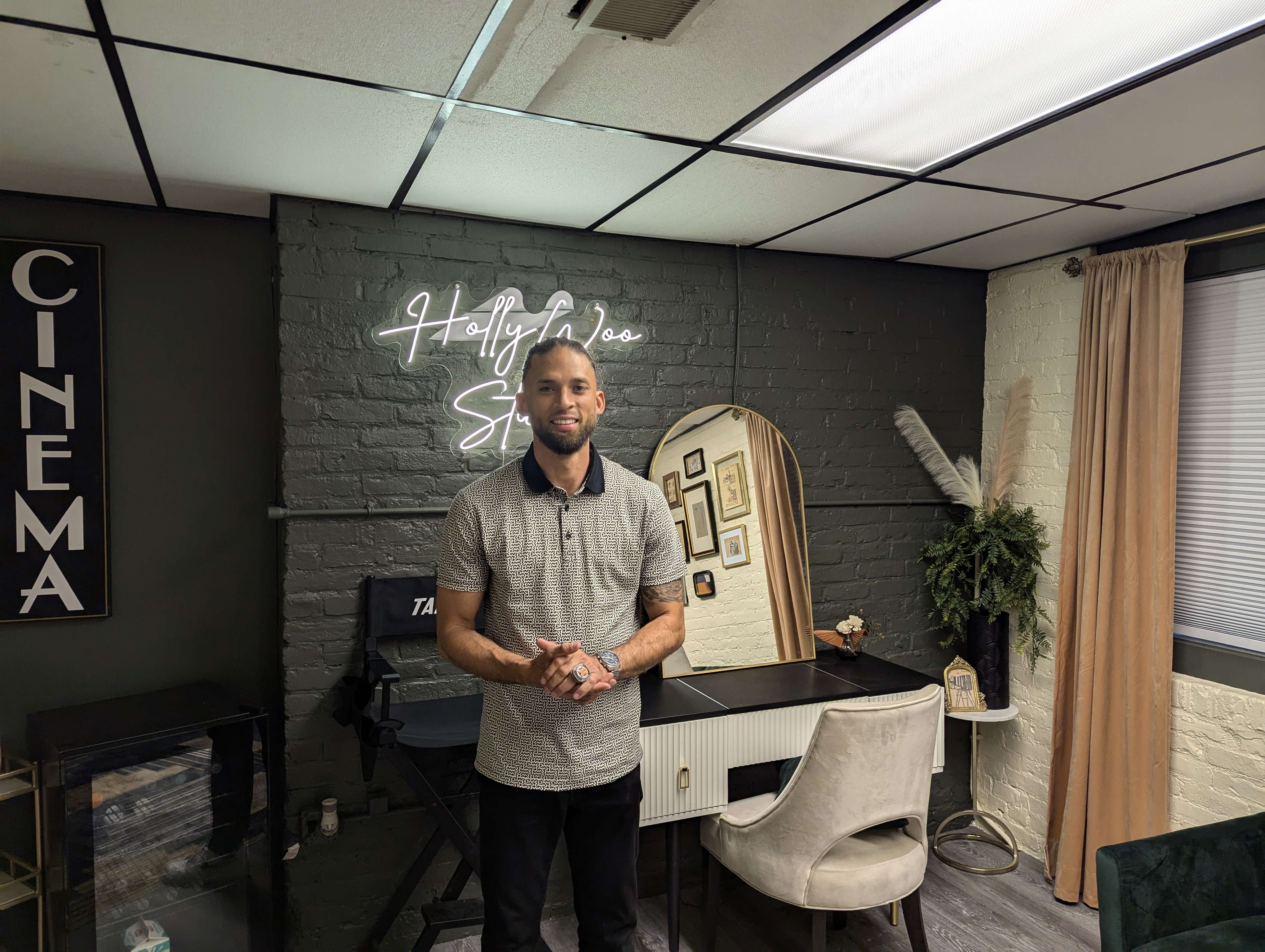 A man stands in a room in front of a neon sign and wardrobe mirror.