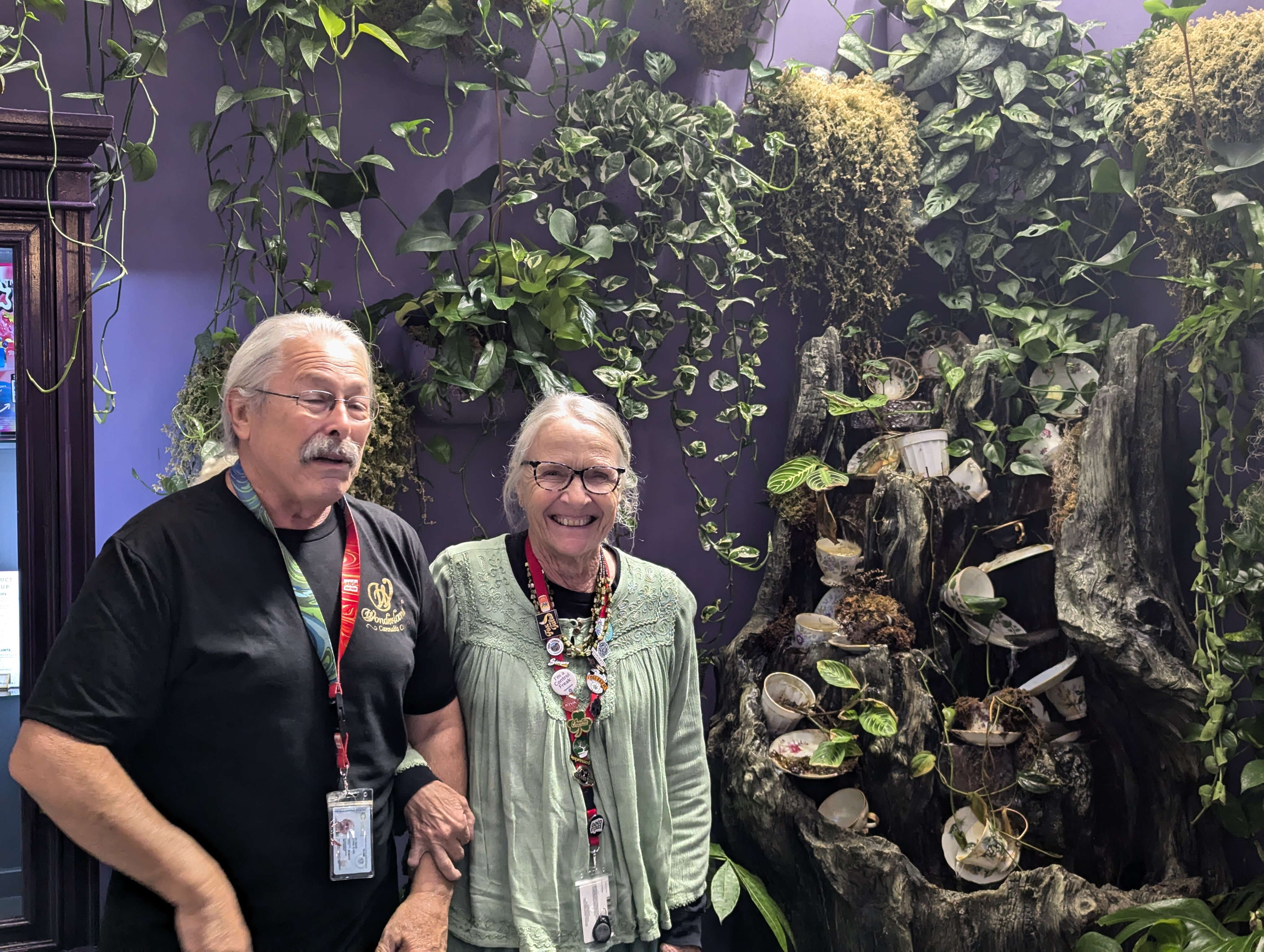 A man and a women stand in front of a water fixture and fake plants