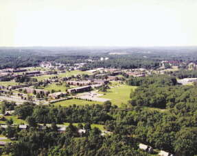 An aerial photo of buildings amongst thickly settled trees and lawns in the 1980s