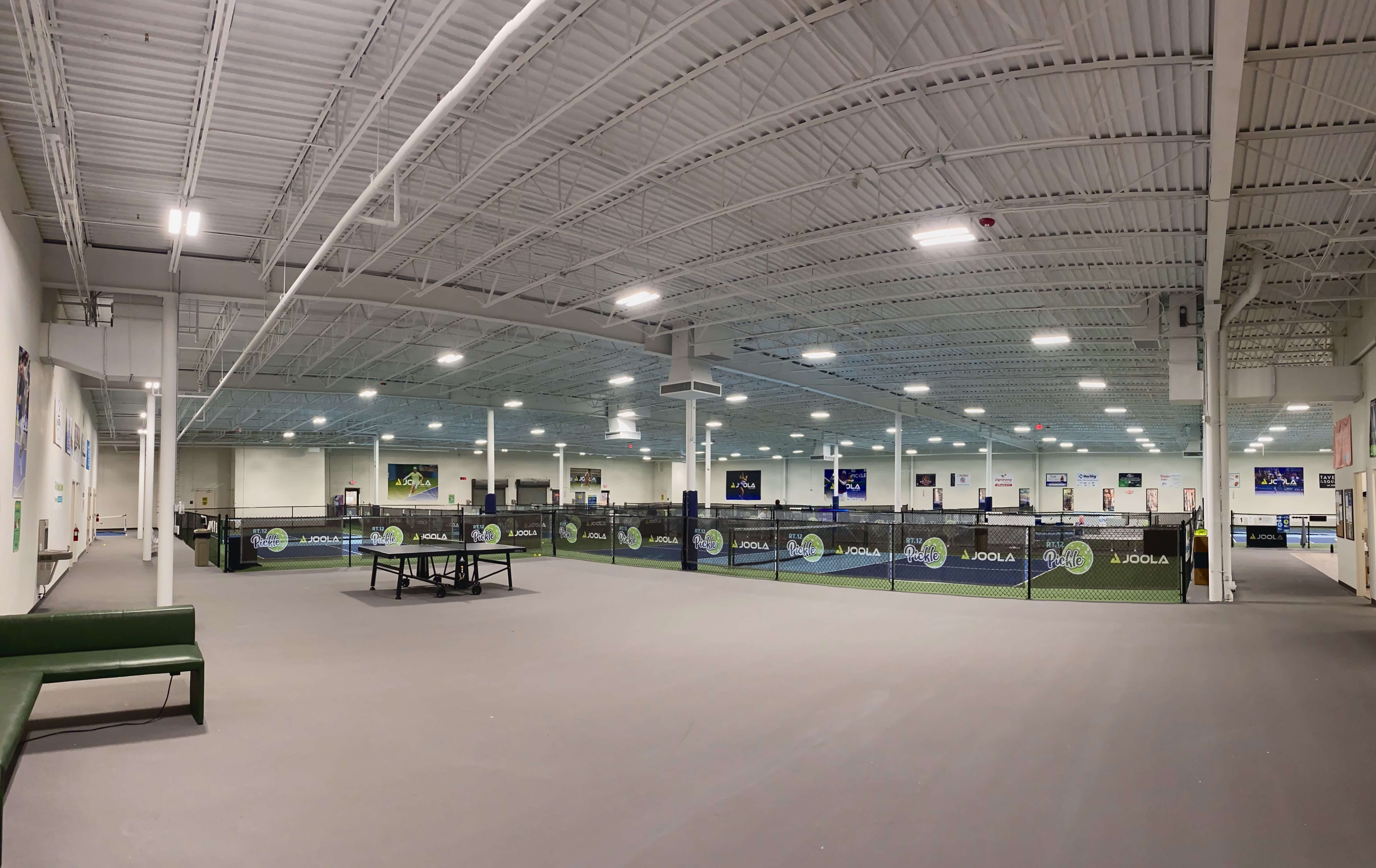 Inside a pickleball court with a grey floor, black nets, and white walls and ceiling