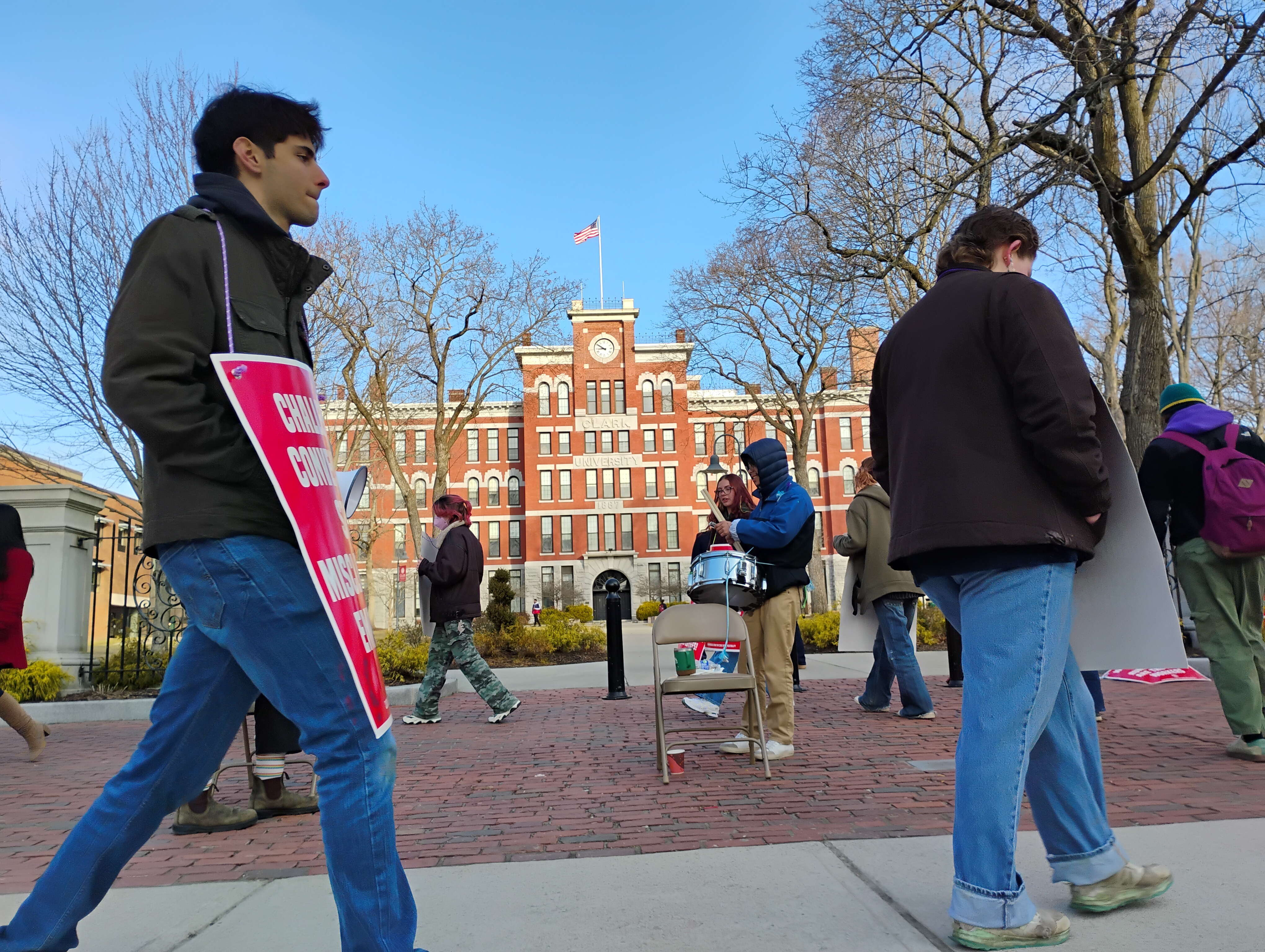 People wearing placards March in a circle in front of an academic building