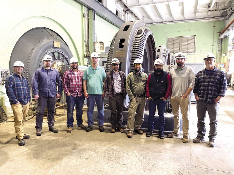 Men in hardhats standing in front of a large power turbine