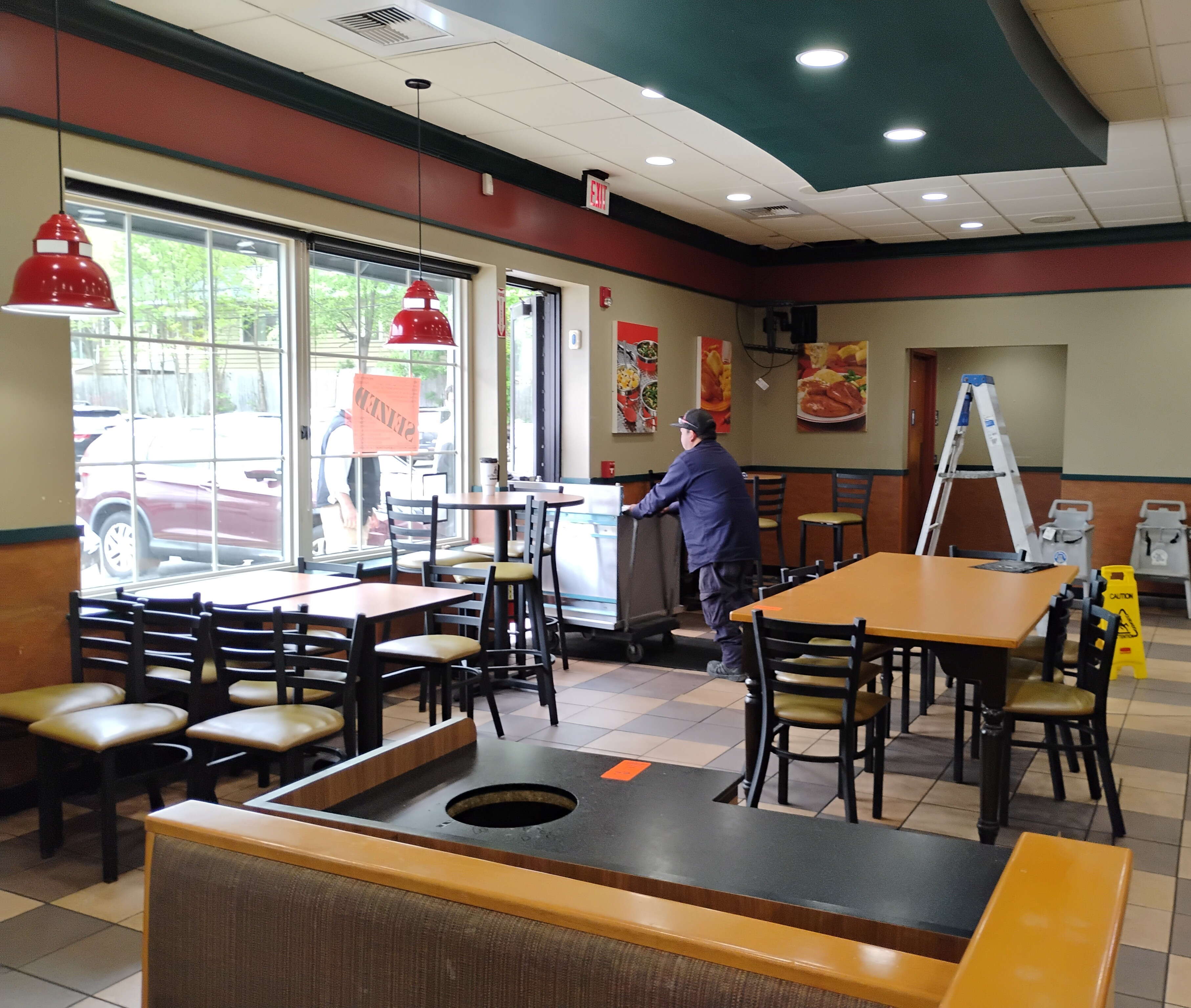 Worker pushing a silver piece of restaurant equipment through a door in a dining room area.  