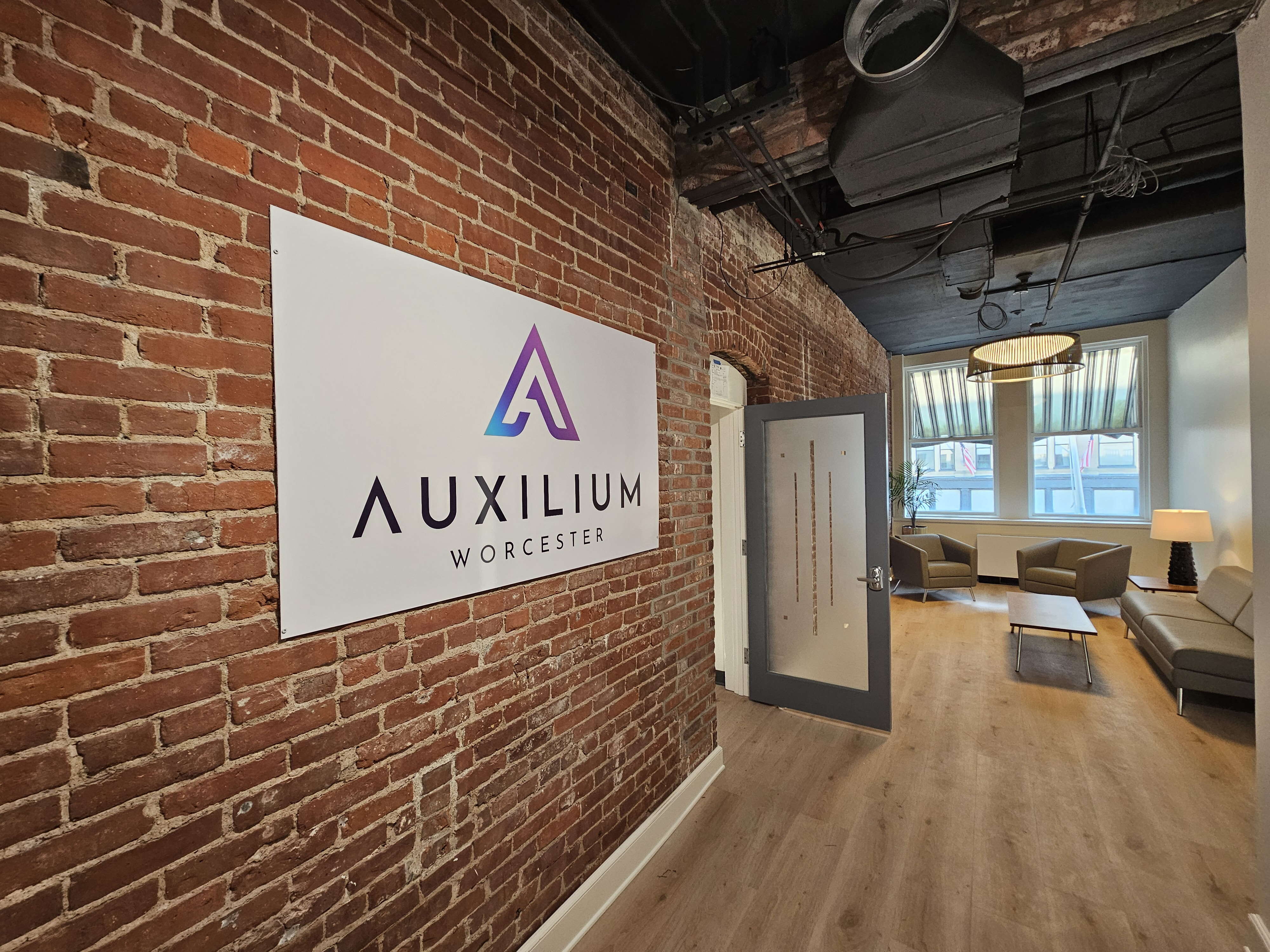 A brick wall with a sign for Auxilium on it in an office-like setting 