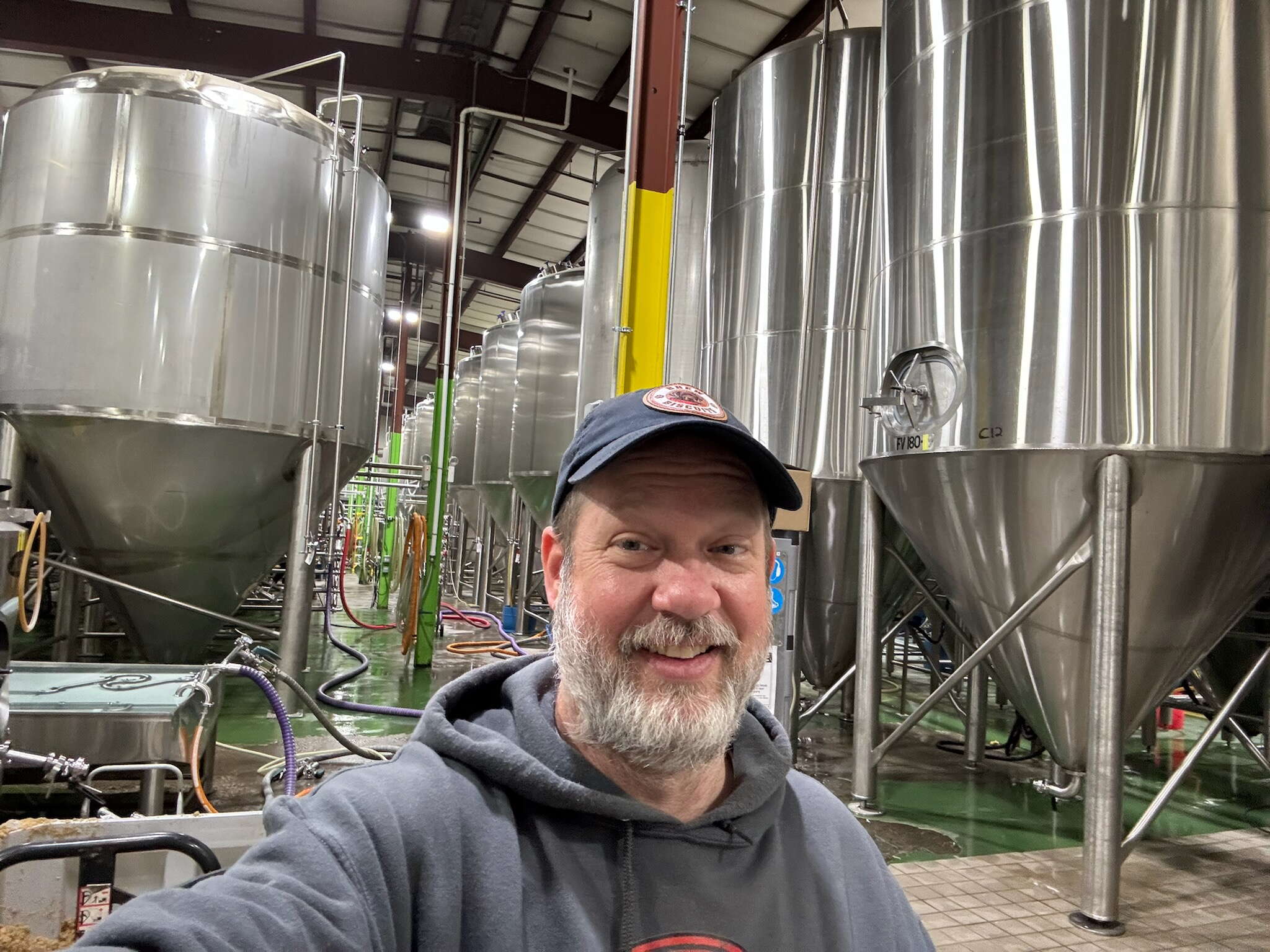 A man wearing a grey hoodie stands inside a brewery.