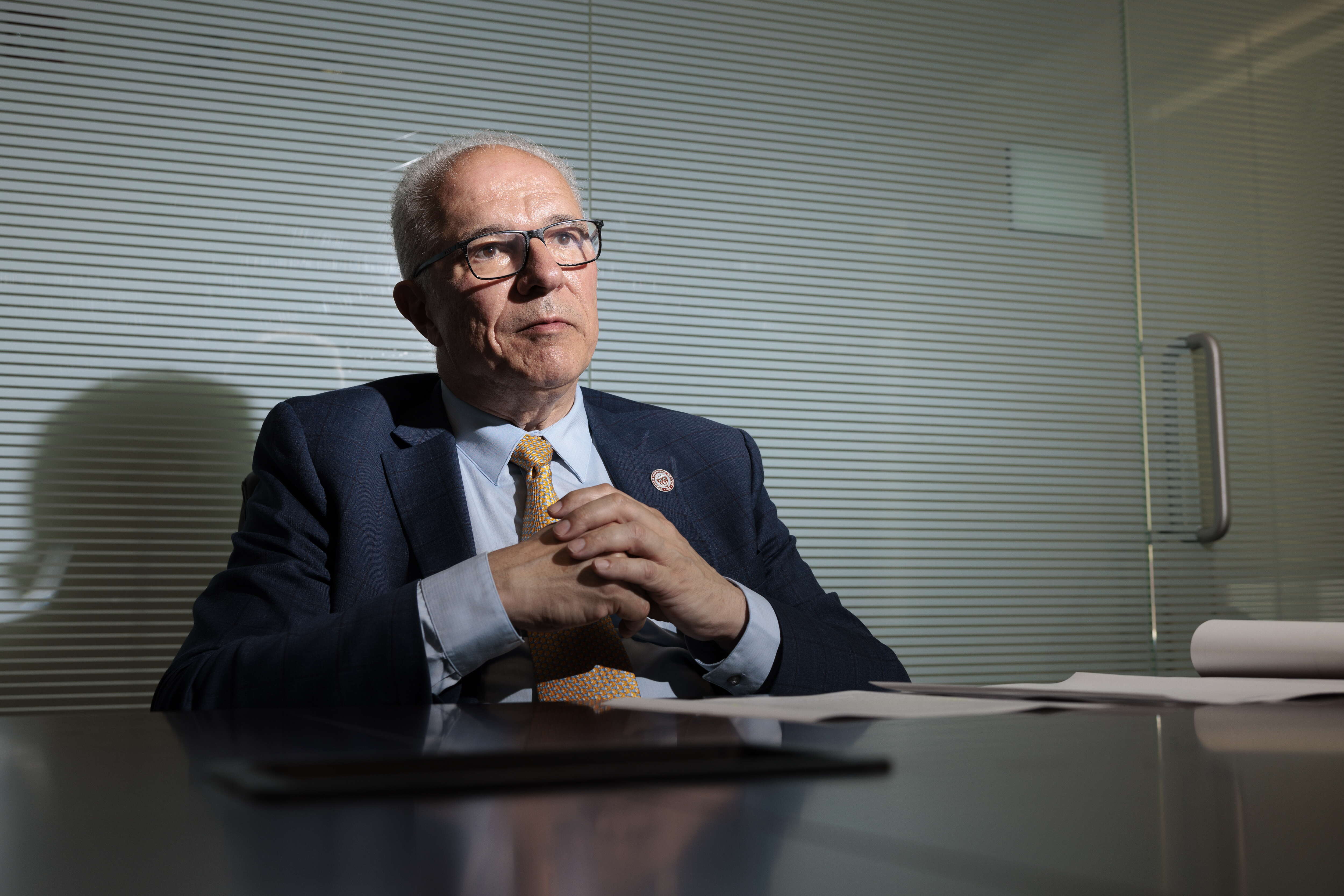 Man in suit sits at a table in front of a glass wall