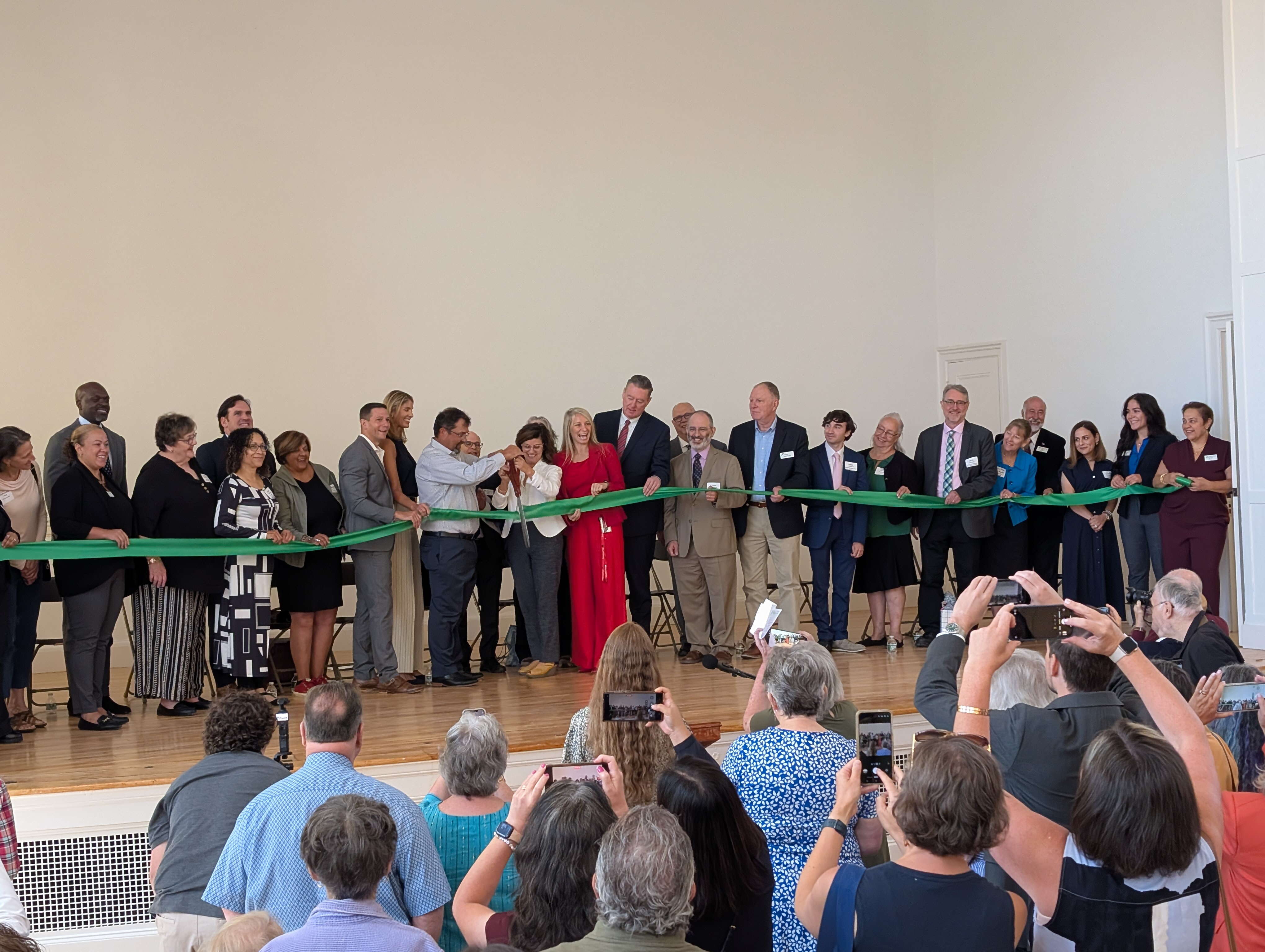 Large group of people gathering behind a green ribbon