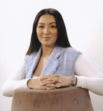 A woman with dark hair wears a light blue jacket and white shirt.
