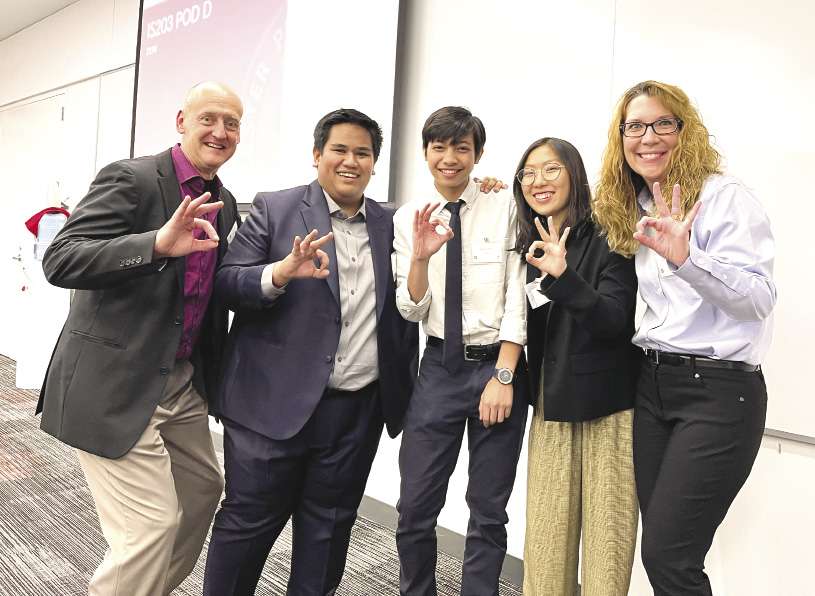 Three student founders are flanked by two mentors. All are making a hand gesture similar to an OK sign.