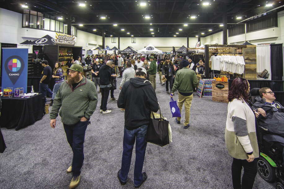 Many people walking around a expo floor, with booths set up on the right and left. 