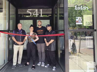 Four people stand in front of a building, with a ribbon cutting