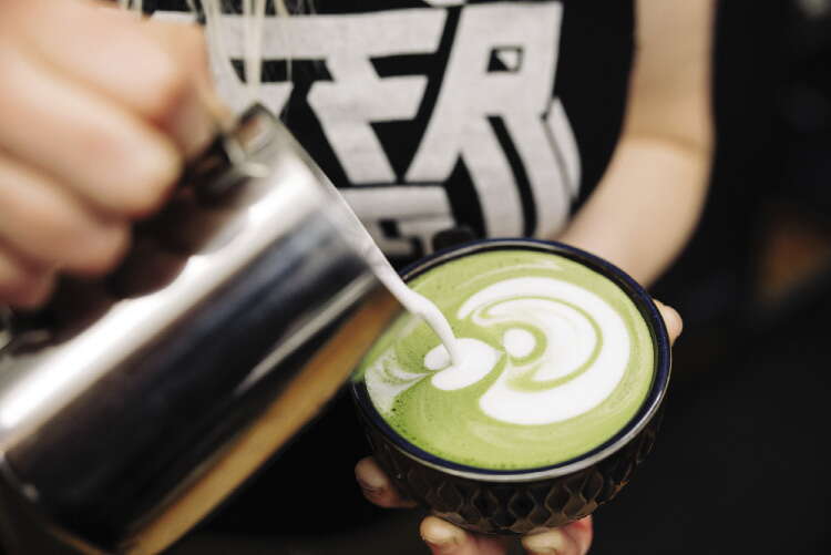 Close-up of a person pouring coffee into a green-colored drink in a mug.