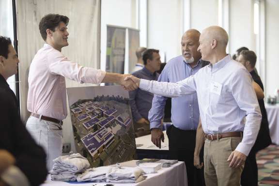 A vendor at the summit shakes the hand of an attendee.