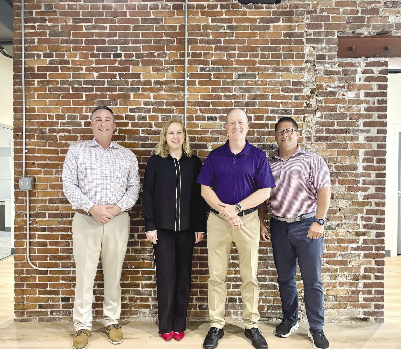 Four people stand side-by-side against a brick wall.