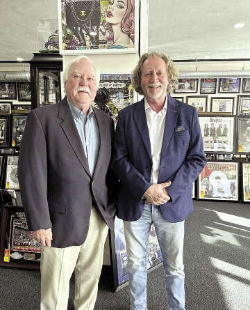 Two men stand in a memorabilia store with framed items behind them