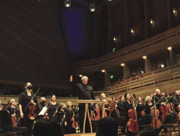 Conductor and orchestra standing with instruments on stage