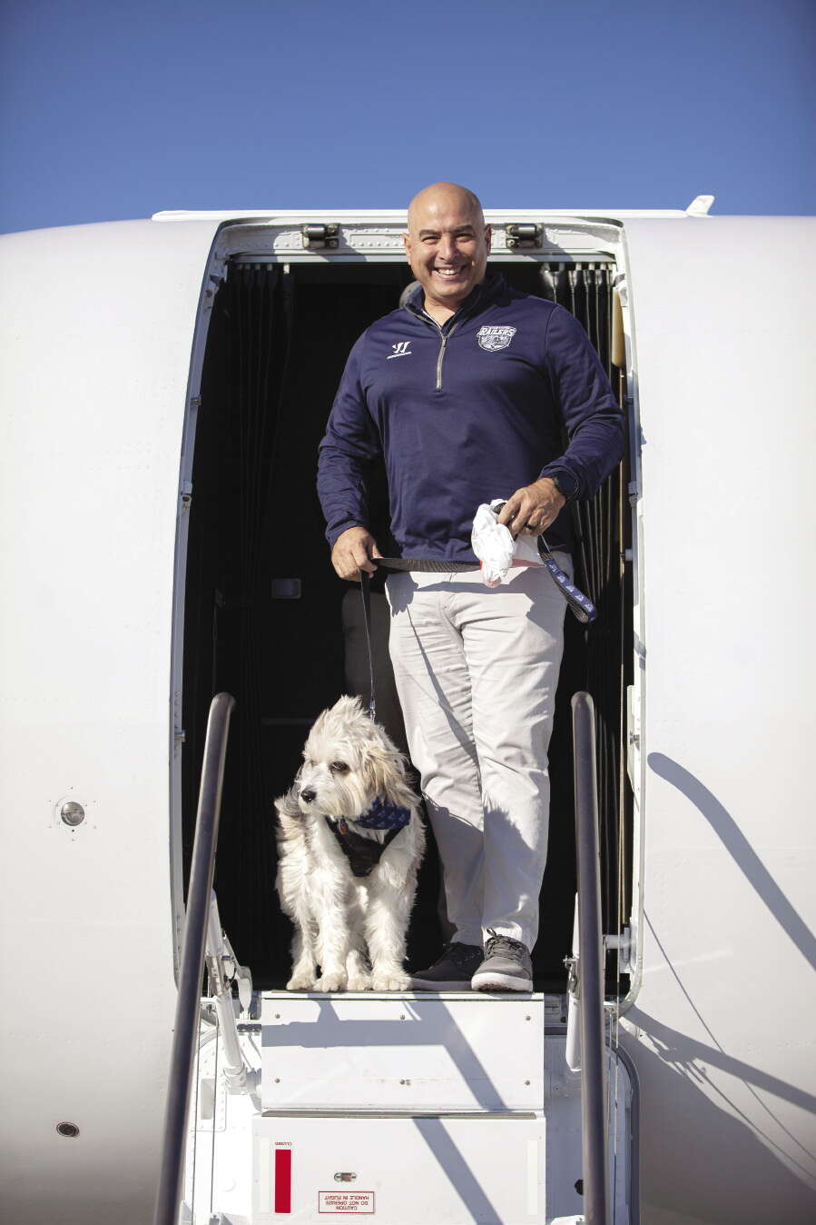 A small white dog and a man stand in the entrance to 