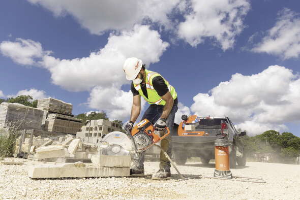 A construction worker uses an electric saw to cut stone outside