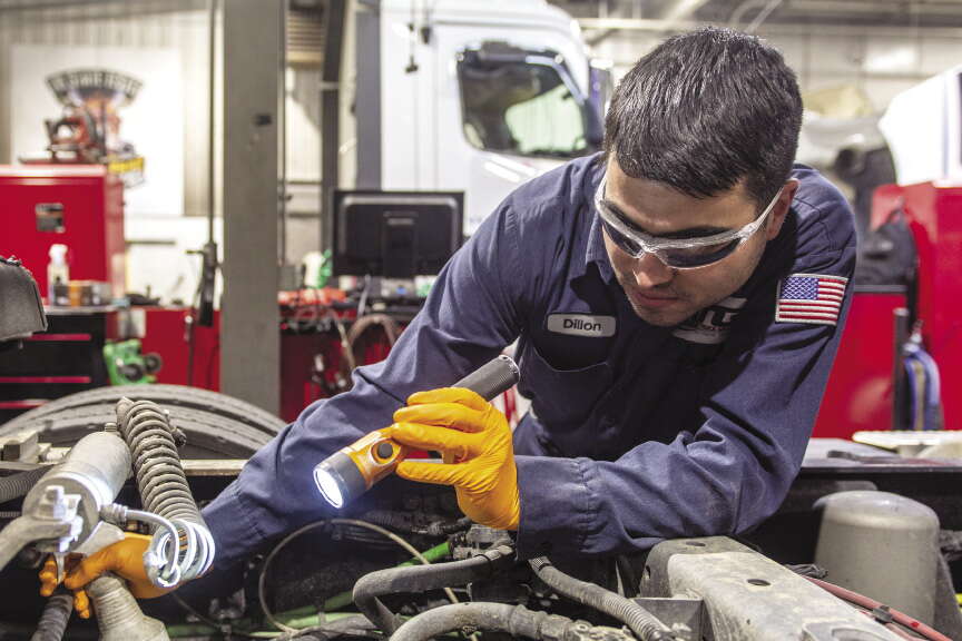 An ATG employee uses a flashlight to look at a truck engine