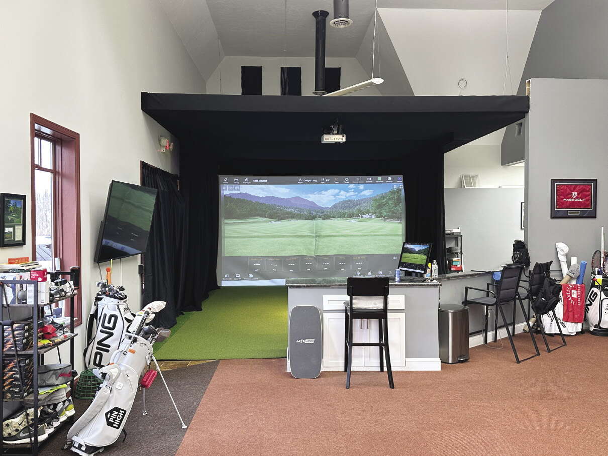 A golf simulator with a bar in front of it and golf equipment to the side