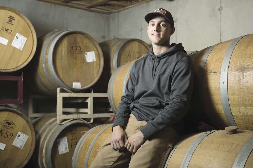 ashoba Valley Spirits' Chief Operating Officer Justin Pelletier sits on oak barrels in the distillery's Bolton facility. .