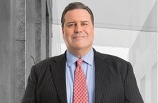 A headshot of a man in a suit wearing a red tie