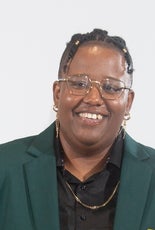 A headshot photo of a woman with a black shirt and green jacket