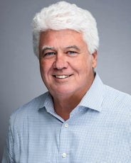 A photo of a man with white hair wearing a white and blue shirt.