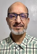 A man wears glasses and a blue, black, and green striped shirt