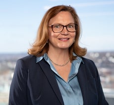 A woman with glasses wearing a blue jacket and a blue shirt looks at the camera.