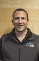 A man in a black shirt against a wood paneled wall.