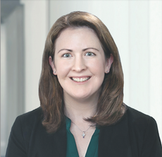A woman with brown hair wears a black jacket and dark green blouse.