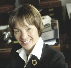 A woman with short highlighted hair wears a black suit jacket and white button down.