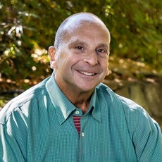 Headshot of a bald man sitting outside with a green patterned button down