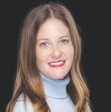 A woman with long blonde hair wears red lipstick and a light blue turtle neck.