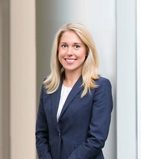A headshot of a woman with blonde hair wearing a dark blue suit jacket and a white top