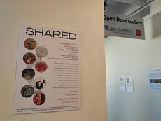 A sign advertising the "Shared" art gallery on a wall outside the gallery space. 