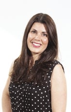 A woman with long brown hair parted in the middle wears a black and white polka dot top.