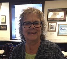 A woman with short grey wavy hair wears a blue cardigan inside a restaurant.