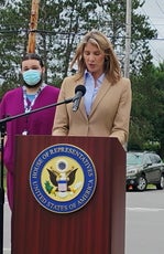 A woman in a beige suit jacket speaks at a podium
